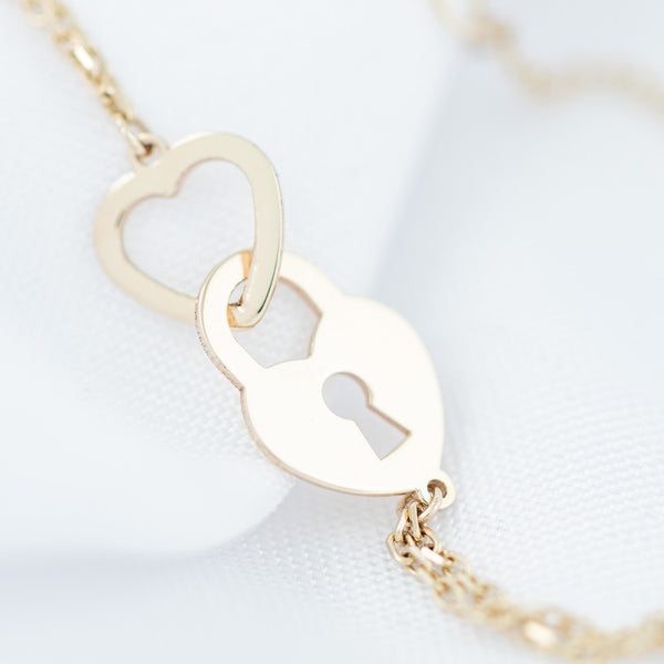 Pulsera eslabón cruzado con aplicaciones motivo corazón y candado de corazón en oro amarillo 14 kilates.