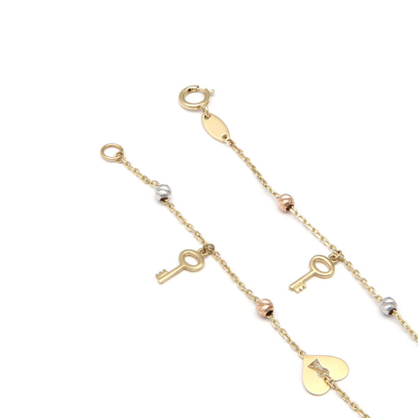 Pulsera eslabón cruzado con aplicaciones y colgantes motivo llaves y corazón en oro tres tonos 14 kilates.