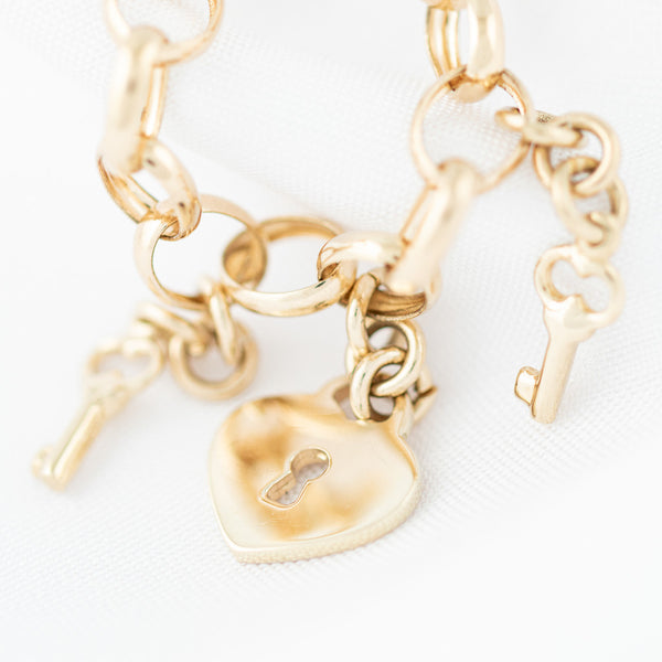 Pulsera eslabón cruzado con colgantes motivo llaves y candado en oro amarillo 14 kilates.