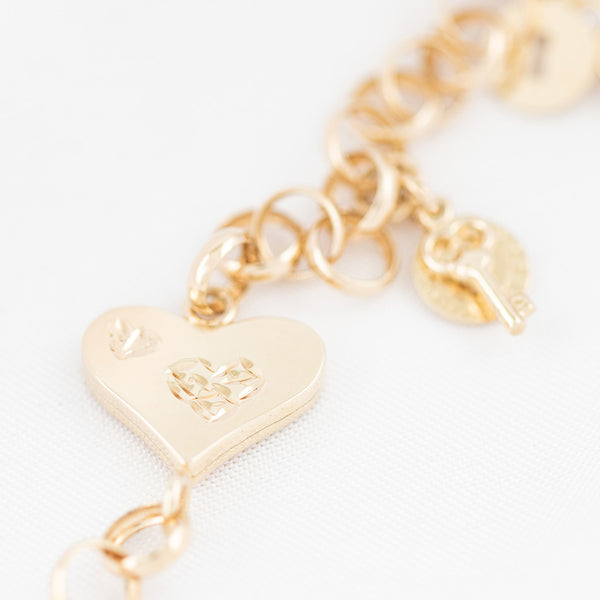 Pulsera eslabón cruzado con aplicación y colgantes motivo candado y llave en oro amarillo 14 kilates.
