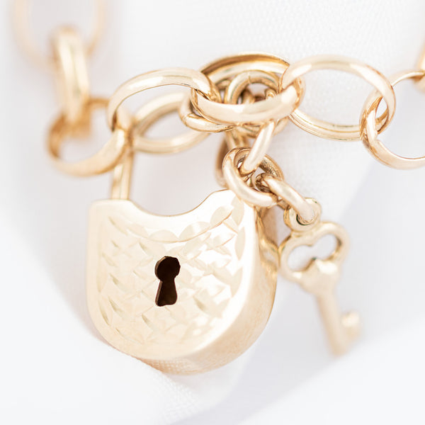 Pulsera eslabón cruzado con colgantes motivo llave y candado en oro amarillo 14 kilates.