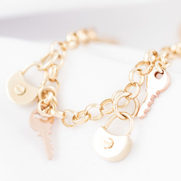 Pulsera eslabón cruzado con colgantes motivos candado y llave en oro dos tonos 14 kilates.
