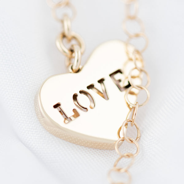 Pulsera eslabón cruzado con colgante motivo corazón en oro amarillo 14 kilates.