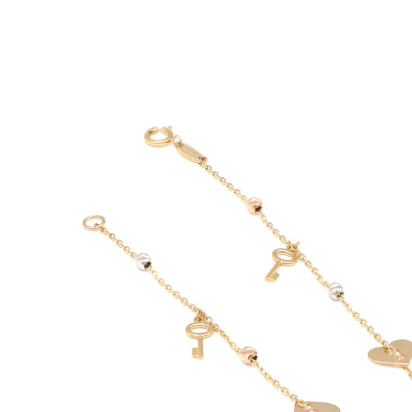 Pulsera eslabón cruzado con aplicaciones y colgantes motivo corazón y llave en oro tres tonos 14 kilates.