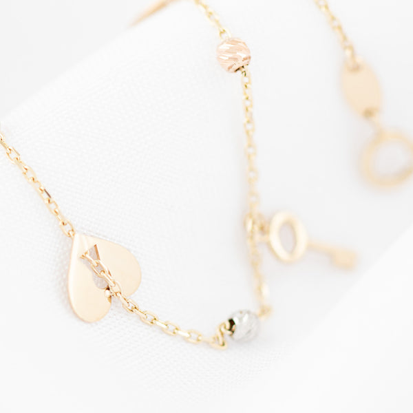 Pulsera eslabón cruzado con aplicaciones y colgantes motivo corazón y llave en oro tres tonos 14 kilates.