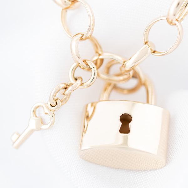 Pulsera eslabón cruzado con colgantes motivo candado y llave en oro amarillo 14 kilates.