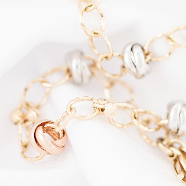 Pulsera eslabón cruzado con aplicaciones motivo nudo en oro tres tonos 14 kilates.