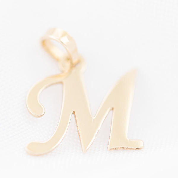 Dije liso motivo letra M en oro amarillo 14 kilates.