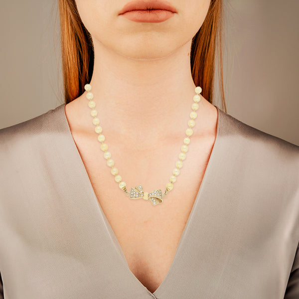 Collar de perlas diseño especial con broche aplicación motivo moño y sintéticos en oro amarillo 14 kilates.