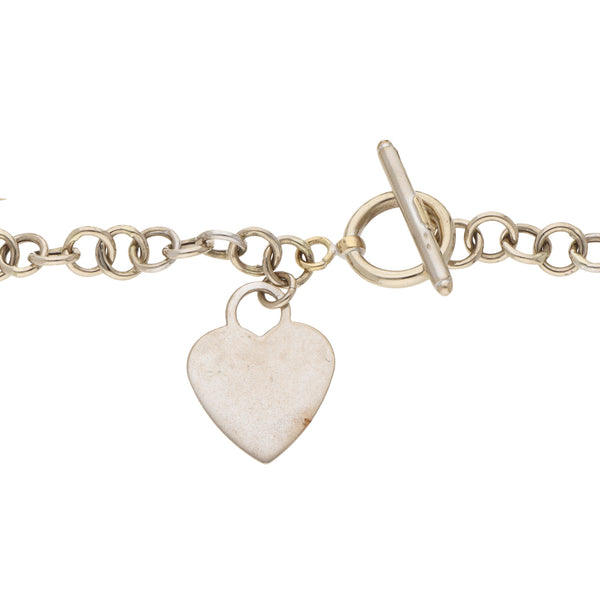 Pulsera eslabón cruzado con dije motivo corazón en oro blanco 14 kilates.