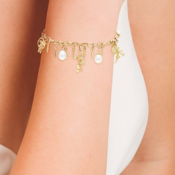 Pulsera eslabón cruzado con dijes motivo hadas y perlas en oro amarillo 14 kilates.