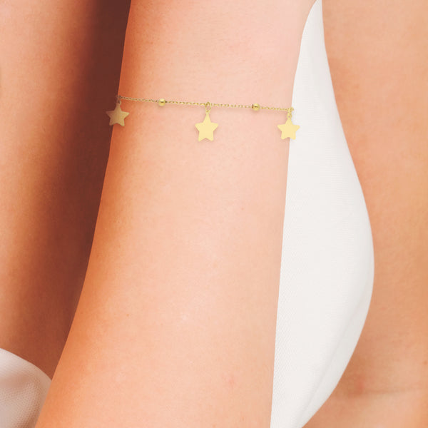 Pulsera eslabón cruzado con esferas y dijes motivo estrella en oro amarillo 14 kilates.