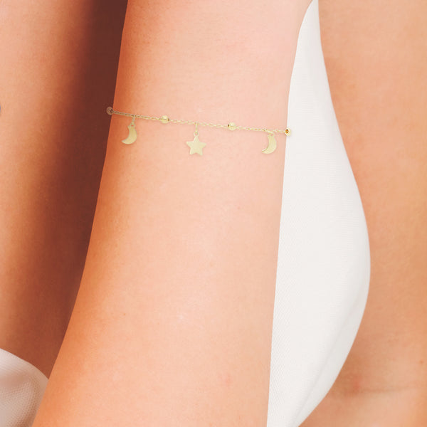 Pulsera eslabón cruzado con esferas y colgantes motivo lunas y estrellas en oro amarillo 14 kilates.